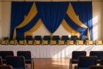 School ceremony hall with blue and yellow drapes and rows of award plaques and medals
