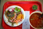 Birria tacos with lime, radish and a cup of consomme on a red tray