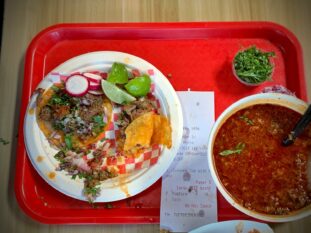 Birria tacos with lime, radish and a cup of consomme on a red tray