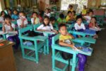 Grade 3 pupils seated at wooden armchairs inside a public elementary school classroom in Nueva Ecija