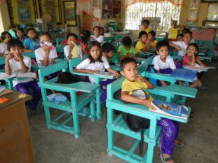 Grade 3 pupils seated at wooden armchairs inside a public elementary school classroom in Nueva Ecija