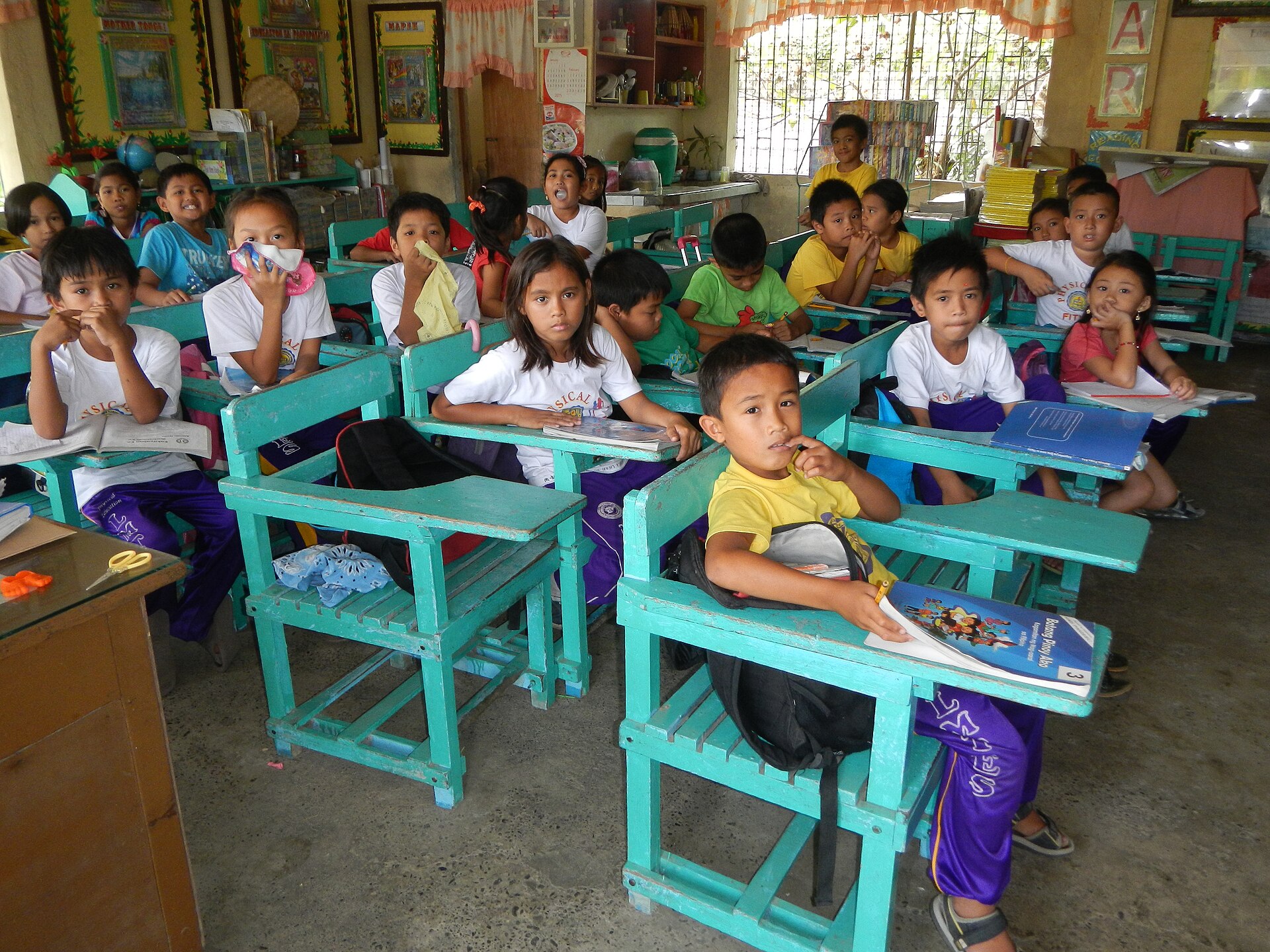 Grade 3 pupils seated at wooden armchairs inside a public elementary school classroom in Nueva Ecija