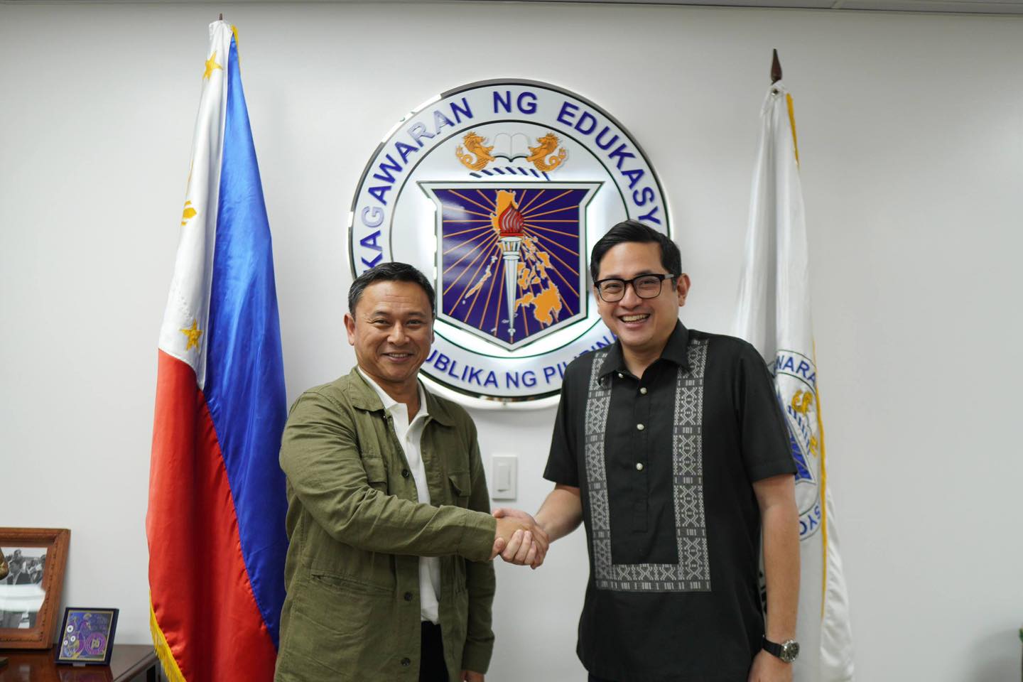 Education Secretary Sonny Angara shaking hands with Sen. Bam Aquino in front of the Department of Education seal