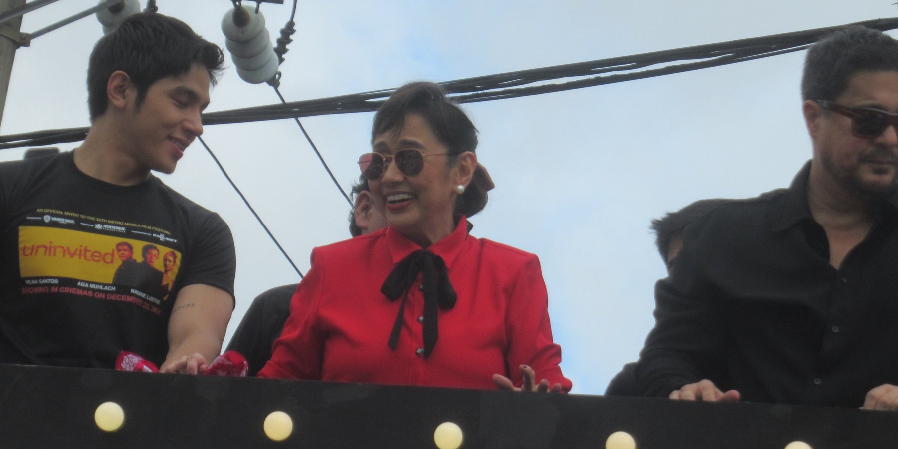 Vilma Santos in a red blouse smiling while on a float at a film promotion